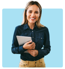 Smiling woman holding a tablet, wearing a dark blue shirt and beige pants, standing against a bright blue background.